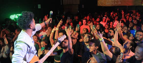Zeruabbel Molla's performing on stage with a guitar, engaging a lively crowd.