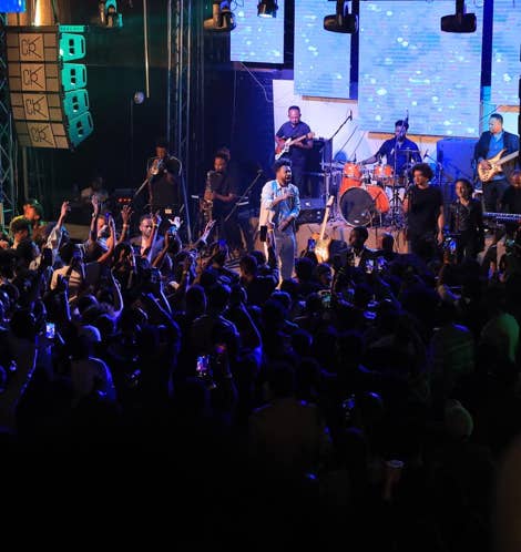 Zeruabbel Molla and a band performing on stage with a large crowd in front, under blue lighting.