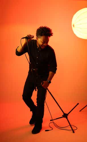 Zeruabbel Molla singing into a microphone on a stand in a red-lit room.