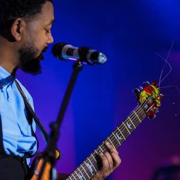 Zerubabbel Molla with Guitar playing guitar and singing into a microphone on stage with blue and purple lighting.